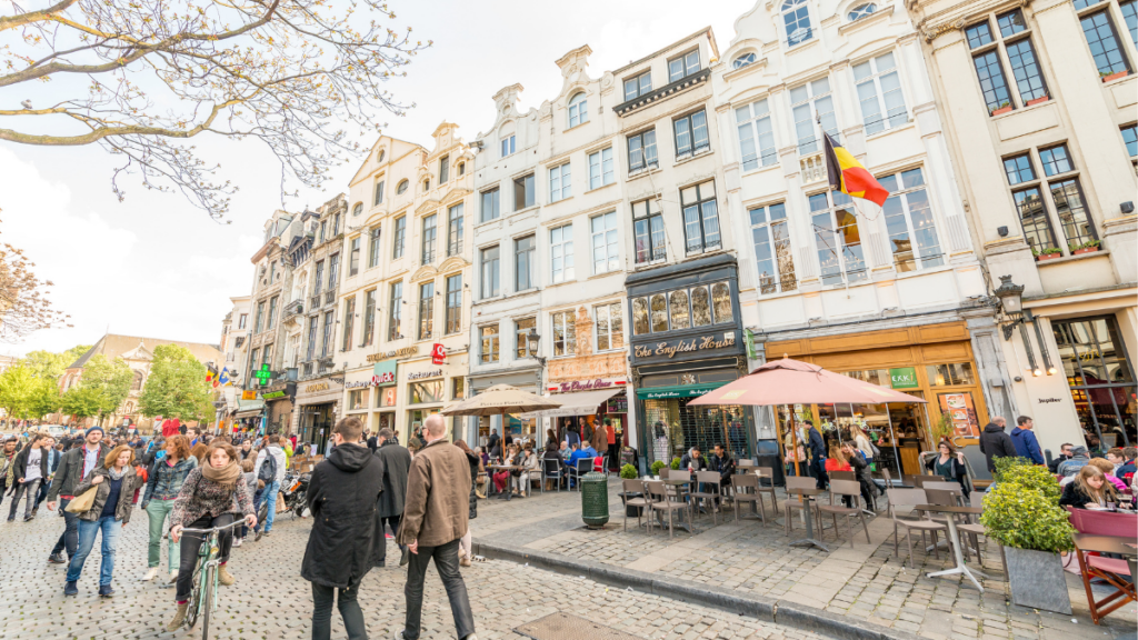 Rue animée du centre de Bruxelles avec commerces, terrasses et passants à quelques pas de la Grand-Place.